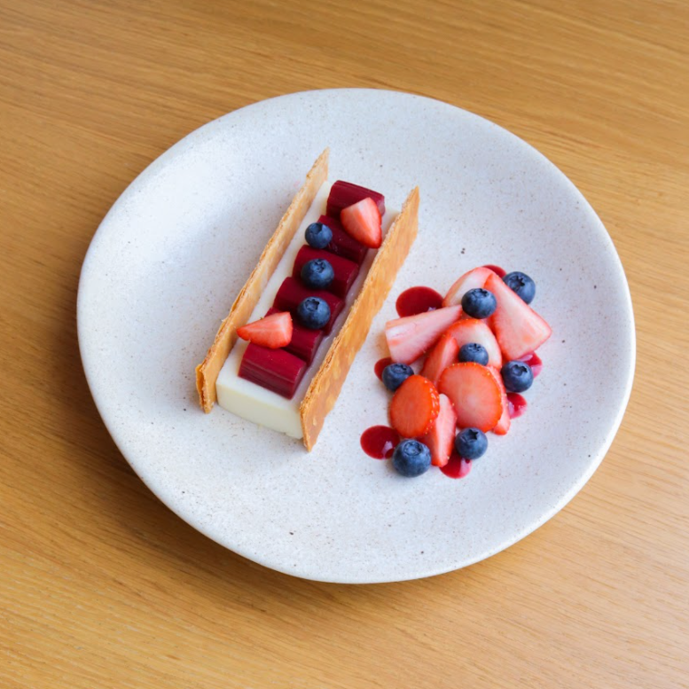 Pochoutka z bílé čokolády s vanilkou, ochucená červeným Kampotským pepřem, pošírovanou rebarborou a macerovanými jahodami